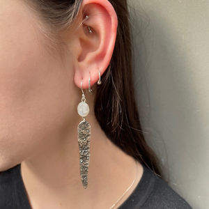 Young women wearing silver earrings with a moonstone.